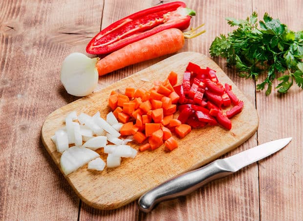 нарезанные морковь, лук и перец на разделочной доске, рядом нож и зелень