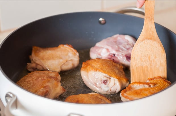 обжаренные куриные бедра в масле на сковороде с лопаткой