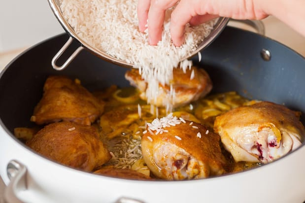сырой рис пересыпается в сковороду с обжаренными куриными бедрами