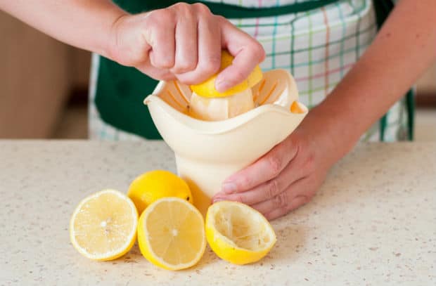 лимон выдавливается через соковыжималку, рядом четыре половинки лимона на столе