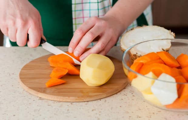 морковь нарезается крупными кусочками, рядом очищенный картофель на разделочной доске и тарелка с картошкой и морковкой на столе