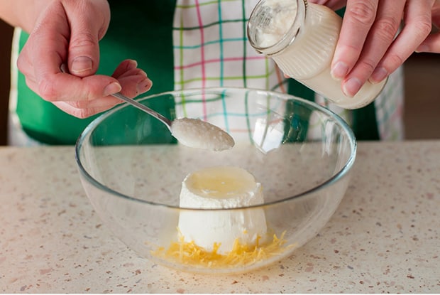 домашний йогурт в баночке и чайной ложке, сливочный сыр с лимонной цедрой в прозрачной тарелке на столе