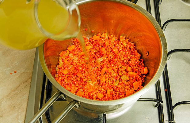 бульон вливается в сотейник с оранжевой чечевицей, луком и морковкой