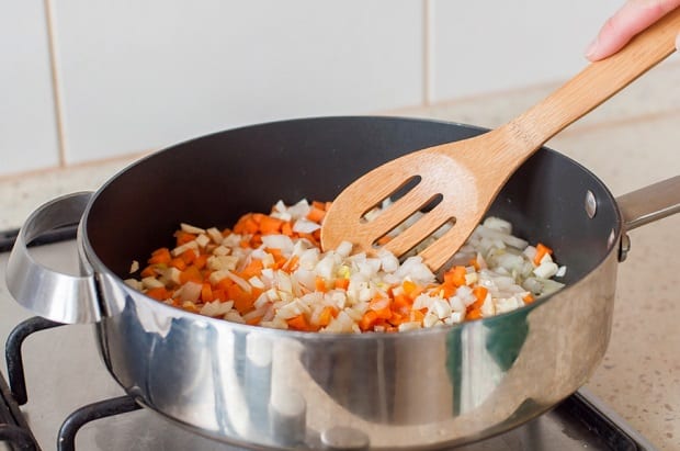 нарезанные кубиками лук и морковка в сковороде с лопаткой на плите
