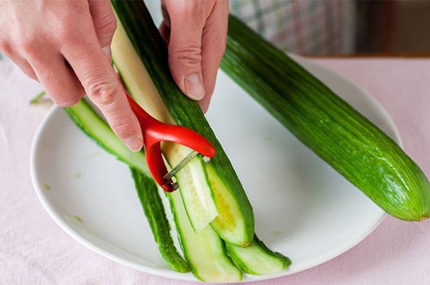 свежий длинный огурец нарезается тонкими слайсами при помощи овощечистки